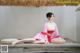 A woman in a pink kimono sitting on a wooden platform.