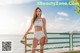A woman in a white bikini standing on a railing by the water.