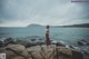 A woman standing on a rock by the ocean.