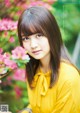 A woman in a yellow blouse sitting in front of pink flowers.